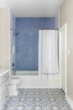 bagno con piastrelle smerlate blu nella doccia, tenda della doccia, piastrelle del pavimento a motivi grigi e blu