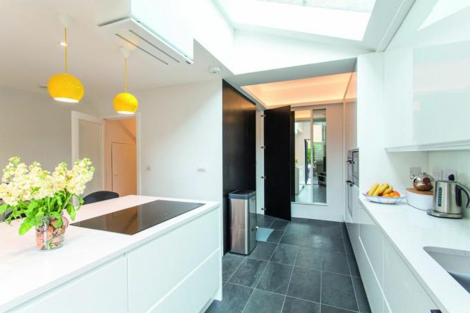 extensão de cozinha contemporânea em retorno lateral com unidades brancas e iluminação suspensa em amarelo brilhante projetada pelo arquiteto de sua casa