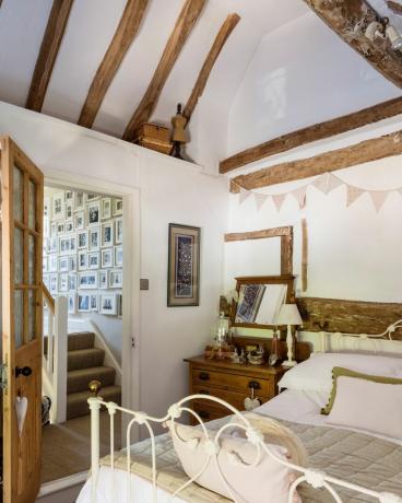 Schlafzimmer mit Originalbalken und schmiedeeisernem Bett in einem Cottage aus dem 17. Jahrhundert