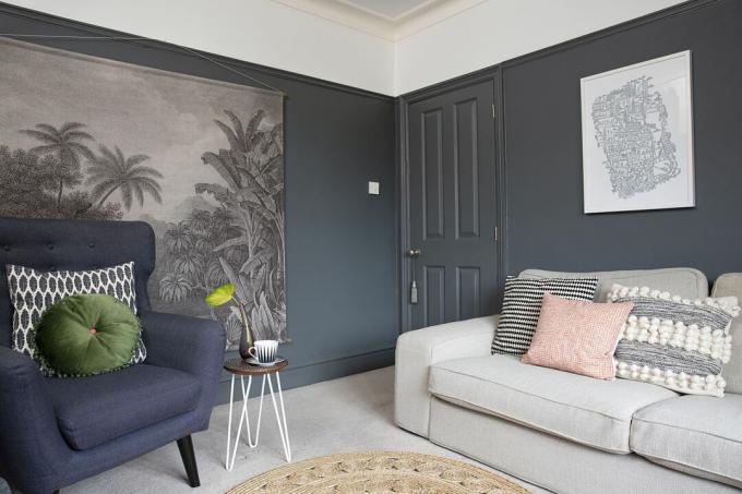 Salon avec murs peints en bleu marine foncé et moquette grise contrastante, un canapé gris avec des coussins rose poudré et un fauteuil bleu