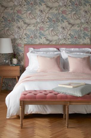 rozā samta gulta ar baltu linu un ziedu tapetēm
