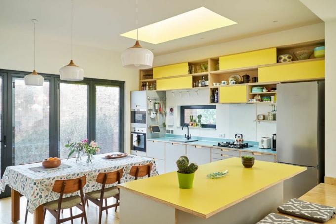 黄色のキャビネット、黄色の調理台、ガラスを備えたオープンプランのキッチンダイナー