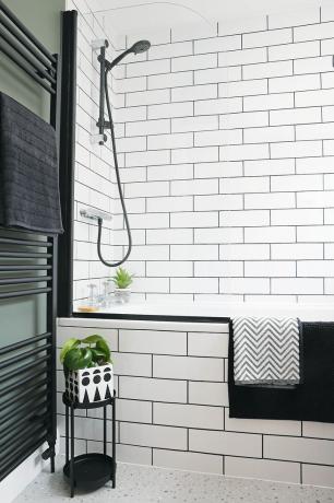 Kylpyhuoneessa valkoiset metrolaatat ja musta saumaus kylvyn ja seinän puolella