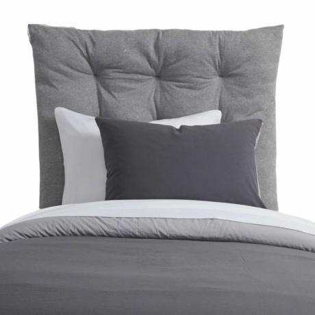 Una cabecera gris con ropa de cama gris y blanca.