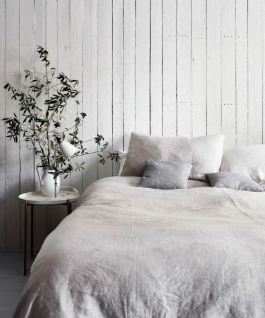 cama com roupa de cama cinza e uma parede shiplap branca