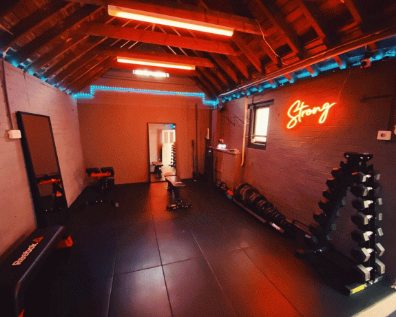 Una palestra di casa con illuminazione d'atmosfera rossa e luce al neon " Strong"