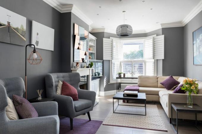 Reforma da sala de estar: sala de estar cinza com janela grande tipo bay window, venezianas brancas, lareiras brancas e sofá de canto cinza