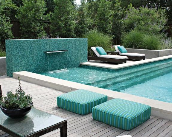 Uma piscina de mosaico azul brilhante com deck de madeira cinza