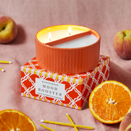 Uma vela laranja cercada por laranjas e maçãs.