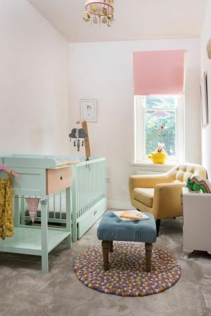 Kinderzimmer mit Pastellfarben, gelbem Stuhl, blauem Hocker, mintfarbenem Kinderbett und rosa Jalousie