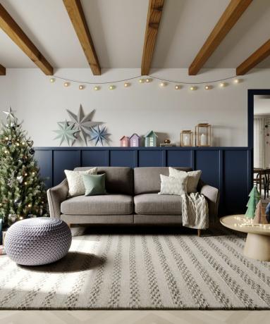 Šedá pohovka vedle vánočního stromku, káva tbale a modrý příborník s barevnými domy