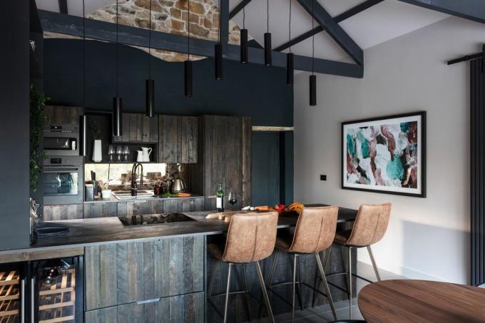 مطبخ ذو ألواح خشبية بنية داكنة وبار إفطار مع مقاعد مرتفعة من الجلد البني وأضواء معلقة سوداء في الأعلى