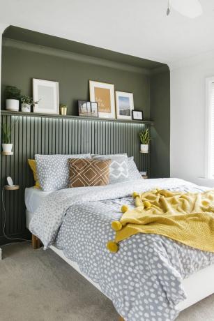 Koyu yeşil tonda boyanmış girintili yataklı yatak odası, resim rayı yüksekliğine kadar ince çıtalı paneller ve üzerinde sanat eserleri bulunan bir raf