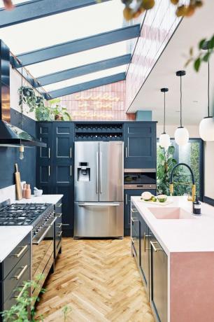 Κουζίνα με διάταξη σε στυλ μαγειρέματος σε προέκταση πλευρικής επιστροφής, με γυάλινη οροφή επάνω, σκούρο μπλε τοίχο και μονάδες και ανοιχτό ροζ νησί