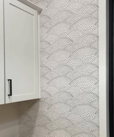 لقطة مقرّبة لخزائن المطبخ البيضاء ذات المقابض ، وديكور ورق حائط أحادي اللون مرقط باللونين الأبيض والأسود