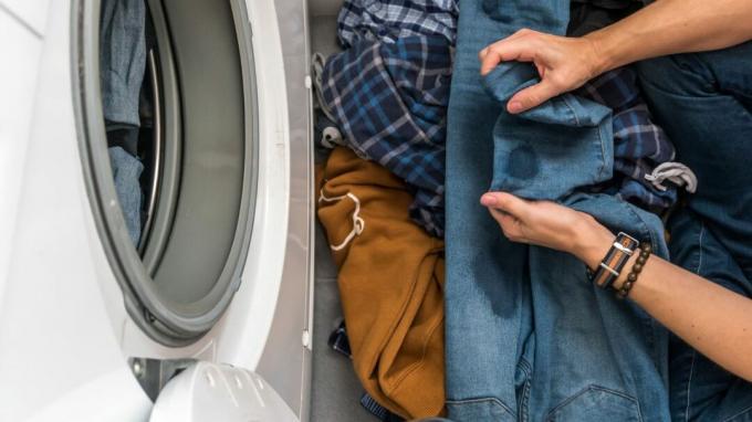 una persona che tiene i jeans macchiati vicino a una lavatrice - GettyImages-1219375328