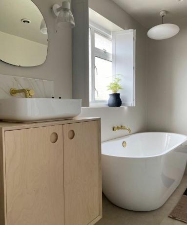 Нейтральная ванная комната со шкафом из светлого дерева, мраморной плиткой и оконными ставнями.
