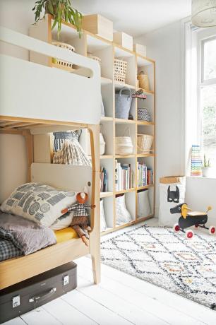 Бяла детска стая с отворени рафтове за дрехи и книги, двуетажно легло в светъл дъб и бяло и едноцветен килим