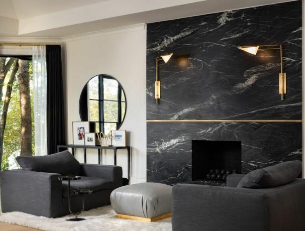 soggiorno nero e crema con parete in marmo nero e poltrone basse nere, poggiapiedi grigio, applique dorate, consolle nera e specchio