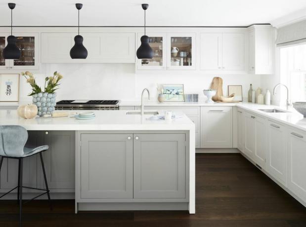 cozinha branca com luzes pendentes pretas, ilha de cozinha cinza, piso de madeira escura