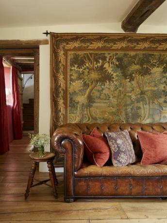 sofá Chesterfield de cuero con cojines rojos frente a un tapiz