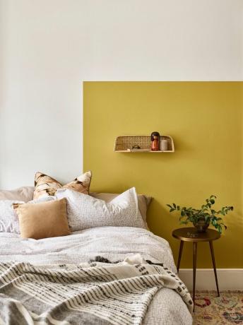 Parete dipinta di giallo dietro il letto con mensola in vimini e arredamento boho