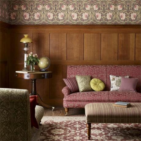 Alacakaranlık pembesi baskılı kanepe ve aydınlatma ve dönem dekoru ile tamamlanmış desenli duvar kağıdına sahip ahşap duvar panelleri