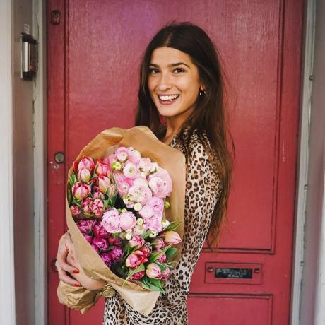 Frau mit Blumen vor einer roten Tür