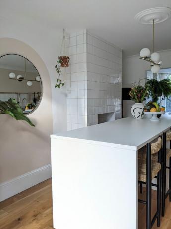 جزيرة مطبخ بيضاء مع مرآة مستديرة على الحائط ونباتات منزلية