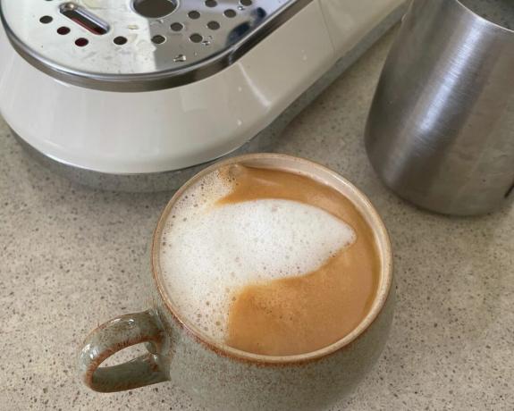 En kopp kaffe ved siden av Smeg-kaffetrakteren med melkekanne i metall