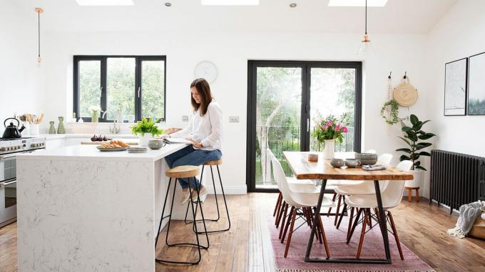 Cucina abitabile a pianta aperta con unità bianche e pavimento in legno