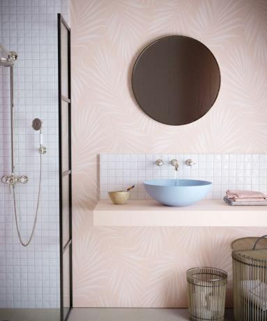 Esquema de banheiro em rosa claro com parede de papel de parede de palma rosa, pia de cerâmica pastel e espelho redondo de parede