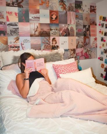 Meitene rozā kopmītņu istabas gultā lasa