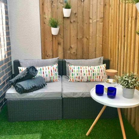 Внутренний двор Airbnb с ограждением, небольшим диваном и искусственной травой