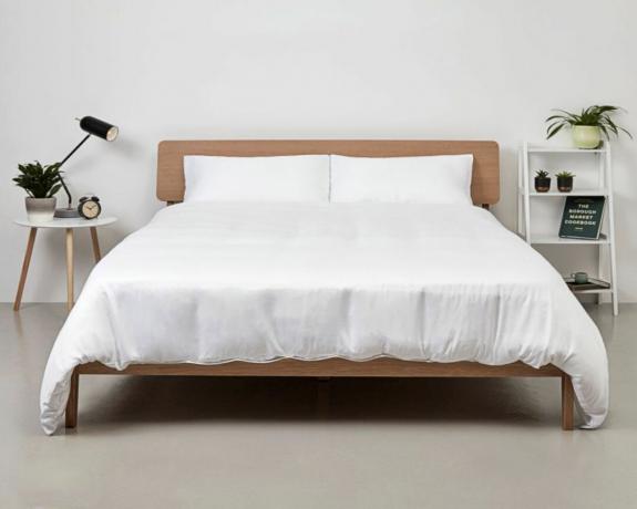 Sänky, jossa puinen sängynpääty, päällystetty valkoisella bambupussilakanalla
