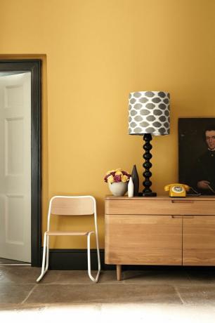 Senffarbene Wand mit Holz-Sideboard und einfarbig gemustertem Lampenschirm