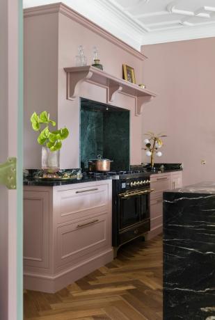 ružičasta kuhinja s pozadinom od zelenog mramora, pločom i otokom od crnog mramora, podom u obliku riblje kosti, štednjakom velikog raspona