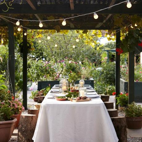 Tavolo da pranzo decorato all'aperto con illuminazione da giardino sotto gazebo in legno