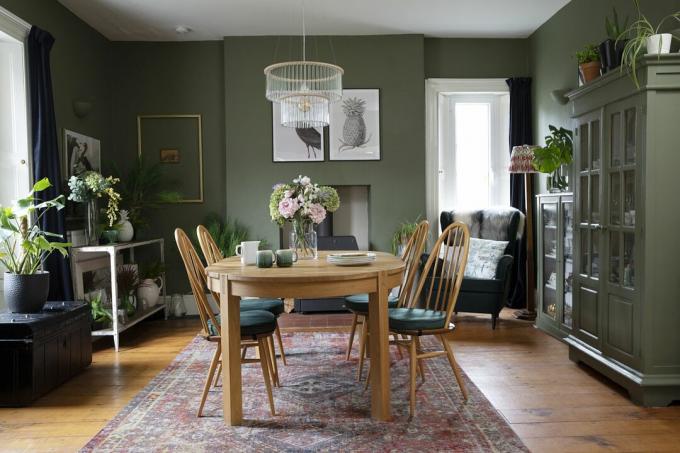 Spisestue med grønne vægge, bordeaux persisk tæppe, lysekrone over spisebord og stole af træ og grønmalet kommode