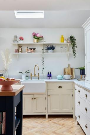 Μια λευκή κουζίνα σέικερ με δύο λευκά ανοιχτά ράφια με φυτά και διάφορα κομψά αξεσουάρ και σκεύη κουζίνας