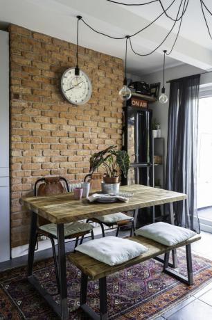 Set da pranzo in stile industriale con robuste gambe in metallo e piano in legno contro una parete effetto mattoni a vista