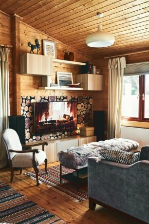 Ein gemütlicher Wohnraum mit Holzimitat-Kulisse, mit Schaffell bezogenem Fußschemel und gebrauchten Möbeln