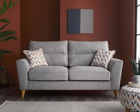 Un divano grigio con piedi in legno in un soggiorno con una parete bordeaux