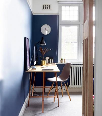 青い壁とスリムな木製の机、灰色のデスクチェアと灰色のカーペットのあるオフィススペース