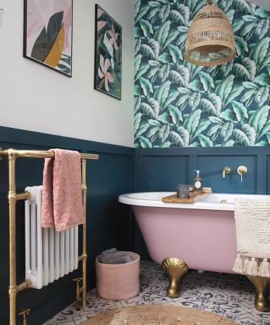Ένα μπάνιο με ταπετσαρία με στάμπα παλάμης, μπλε επένδυση τοίχου, ροζ μπανιέρα, αμπαζούρ από γιούτα και χαλί από γιούτα