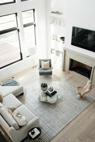 ruang tamu putih dengan furnitur netral, meja kopi kaca, permadani, rak putih
