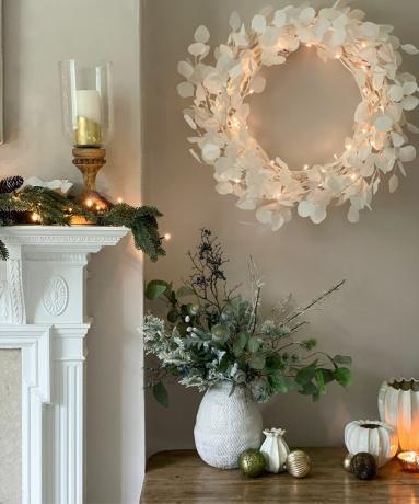 Ruang tamu Natal minimalis dengan perapian putih, karangan bunga Natal, dan dekorasi di atas meja