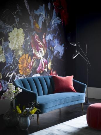 Sininen kukka -seinämaalaus, jossa tumma sinivihreä sohva ja punainen samettityyny