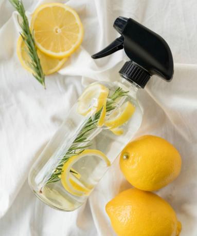 Uma garrafa de vidro de spray ambiente de limão com limões ao redor
