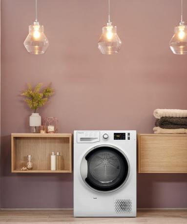 Μια συσκευή πλυντηρίου ρούχων σε δωμάτιο πλυντηρίων με τρίο κρεμαστά φωτιστικά με απαλό ροζ διακόσμηση τοίχου